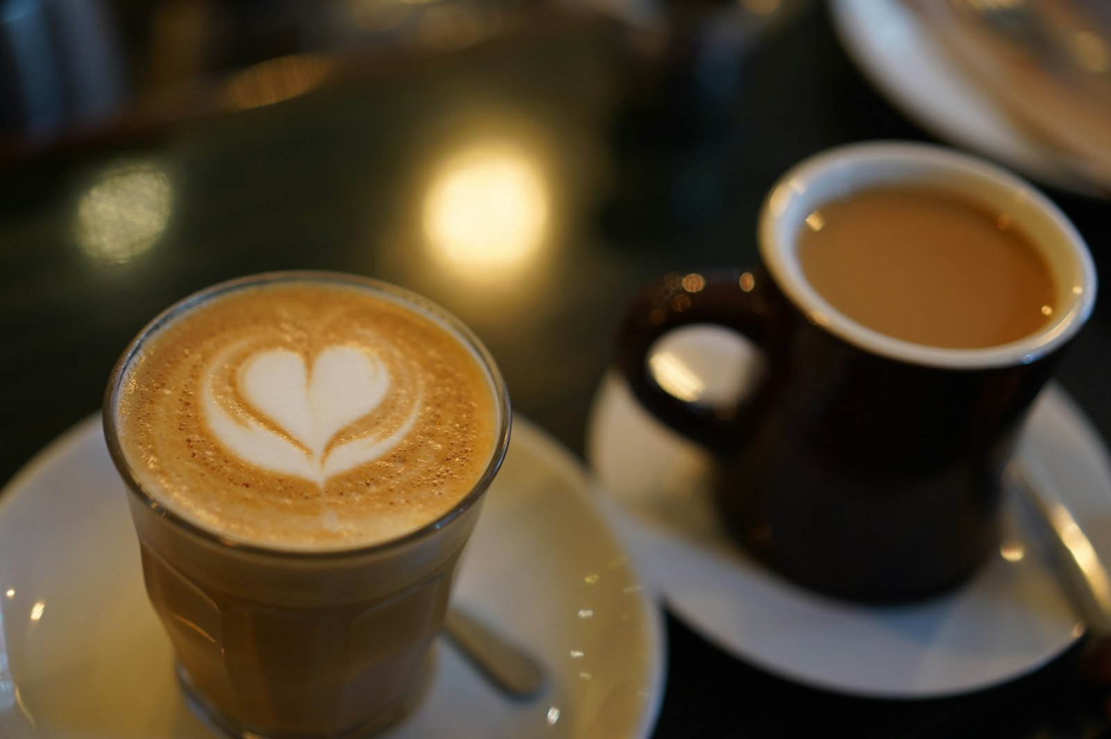 Two cups of coffee on a café table, one with heart-shaped latte art